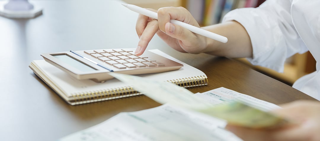 계산기를 사용하고 공책에 글을 쓰는 사람의 클로즈업으로, 재정 계산을 나타냅니다.