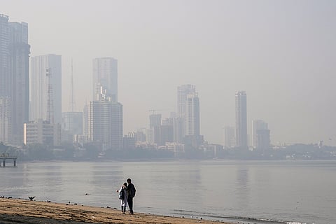 People walk along the seashore as skyline fades into a thick haze in the backdrop, in Mumbai.