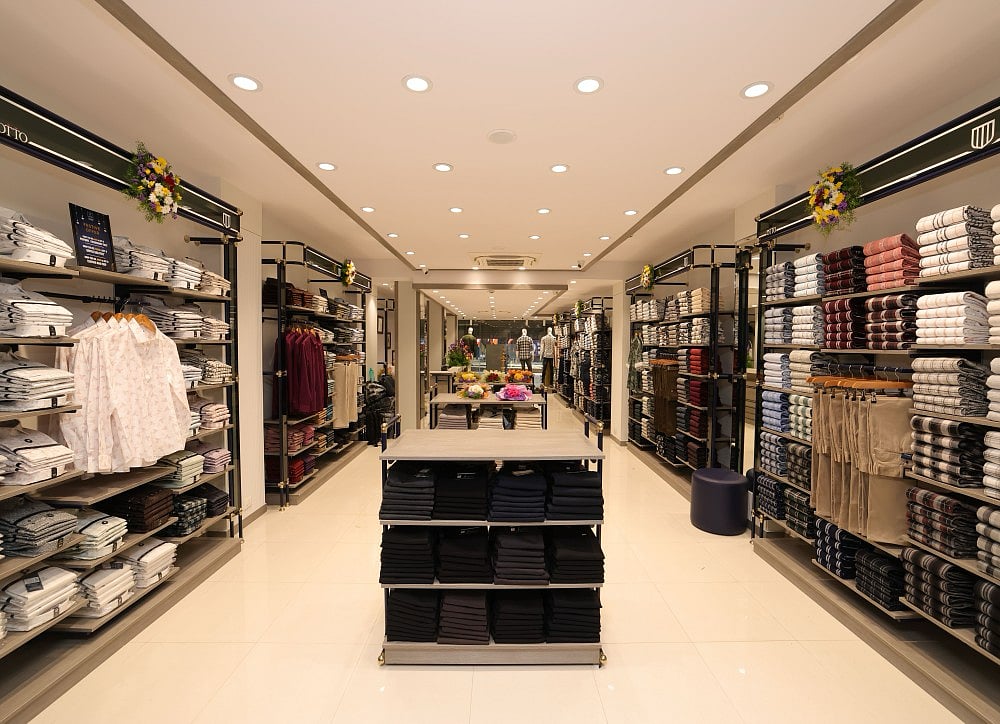 Interior view of a clothing store aisle with shelves of folded shirts and a central display.
