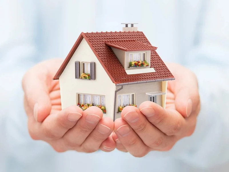 Hands holding a miniature house model with a red roof