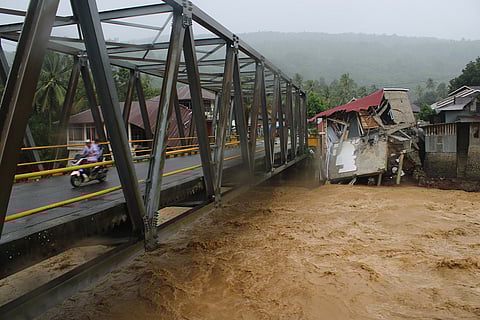 Motorists ride on a bridge past buildings damaged by flooding in Tanah Datar, West Sumatra, Indonesia.