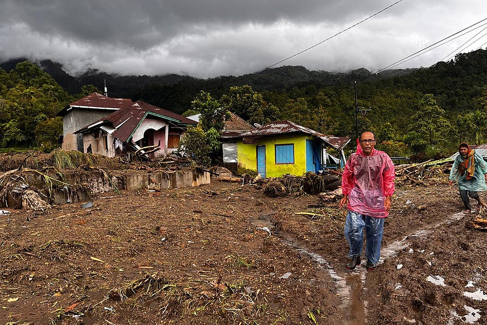 People walk past damaged houses at a village affected by flood in Malalak, West Sumatra, Indonesia. - | Photo: AP/Ade Yuandha