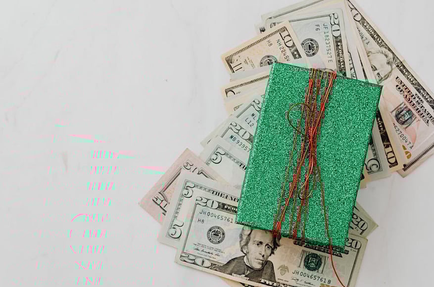 Teal, glittery gift box with red string on a fan of US dollar bills.