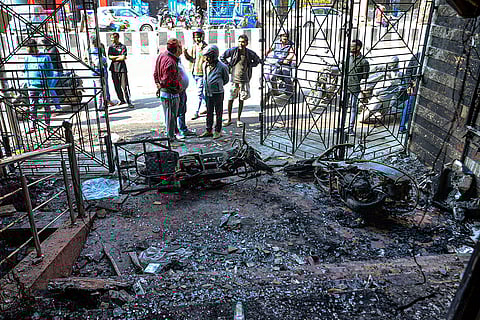 People stand near the charred remains of vehicles after a fire broke out outside a shop, in Ranchi.