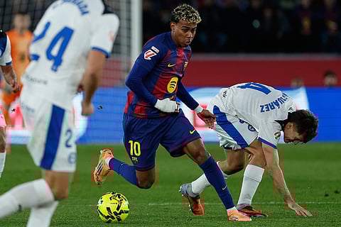 Barcelona's Lamine Yamal, center, vies for the ball with Alaves' Denis Suarez during a Spanish La Liga soccer match between Barcelona and Alaves, in Barcelona, Spain.