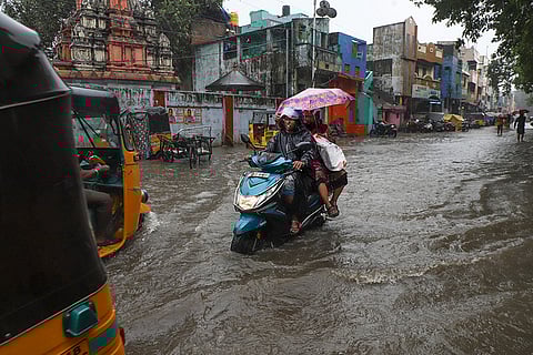 People wade through waterlogged road amid heavy rainfall in the wake of Cyclone Ditwah, in Chennai.