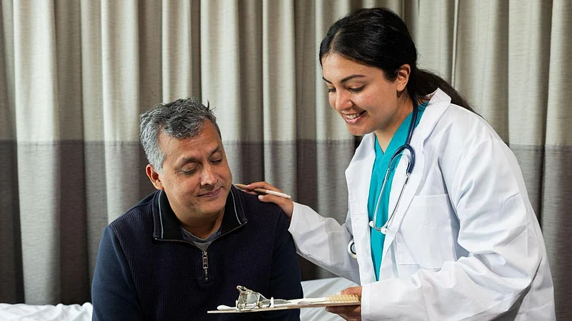 A smiling female doctor consults with a seated male patient in a hospital room