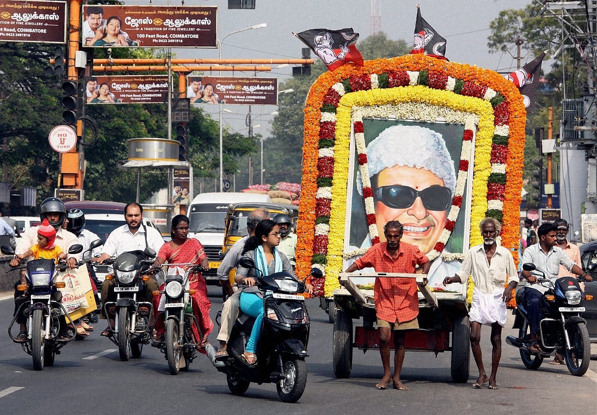 Coimbatore: Two fans of MG Ramachandran (MGR), former Chief Minister of Tamilnadu, ferry his life-size poster through a street to mark his 25th death anniversary in Coimbatore on Monday. - PTI Photo