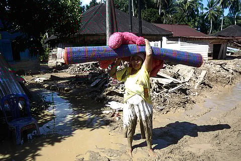 A flood survivor carries a mat as she cleans up her house at a village affected by flash flood in Batang Toru, North Sumatra, Indonesia.