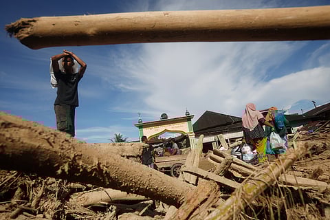Survivors walk past logs swept away by a flash flood in Batang Toru, North Sumatra, Indonesia.