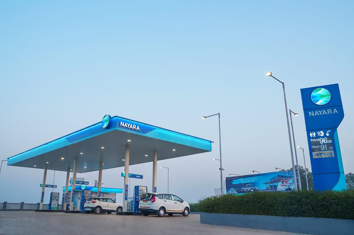 Blue-lit fuel station at dusk with cars parked near the pumps.