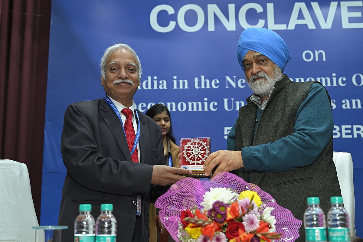 Two men on a stage, one in a suit and one in a turban, exchanging a small memento.