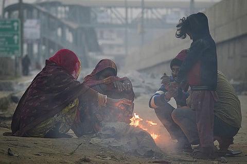 People sit around a small fire to warm themselves on a winter morning, in Gurugram.