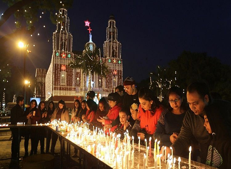 People lighting candles in front of a brightly lit, ornate church building at night