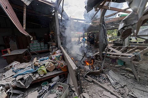 A Thai police officer splashes water to control fire at a house which, Thai local security forces say, was damaged by a Cambodian artillery strike in Surin province, Thailand.