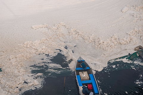 People attempt to remove the thick layer of toxic foam covering the Yamuna river, at Kalindi Kunj in New Delhi.