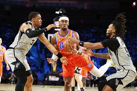Oklahoma City Thunder guard Shai Gilgeous-Alexander, center, tangles with San Antonio Spurs' Keldon Johnson (3) and Stephon Castle (5) under the net in the first half of an NBA Cup semifinals basketball game in Las Vegas. 