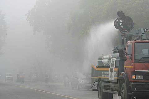 A municipal truck sprays water on a roadside to suppress dust and pollution amid dense foggy conditions, in New Delhi.
