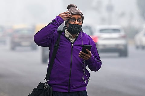 A pedestrian walks through fog on a cold winter morning, in New Delhi.