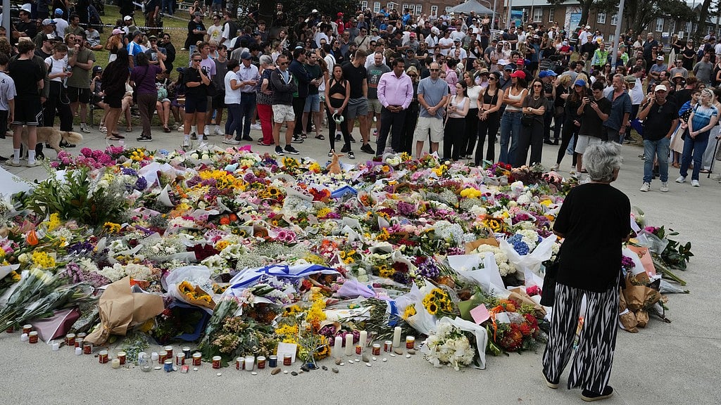 People gather at a growing flower memorial to shooting victims outside the Bondi Pavilion at Sydney's Bondi Beach. - AP