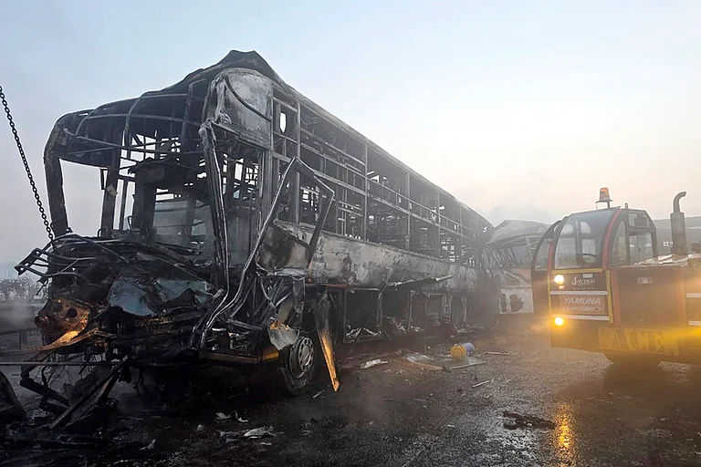 Cranes clear the charred remains of buses after a fog-hit pile-up involving several buses and cars triggered fires on the Yamuna Expressway, in Mathura. - | Photo: PTI