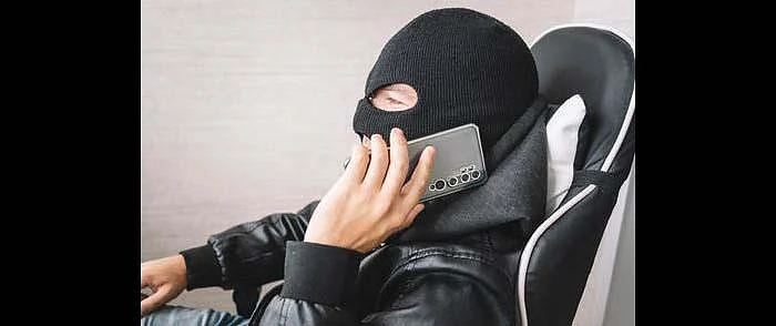 검은색 바라클라바를 쓴 사람이 의자에 앉아 통화하고 있습니다