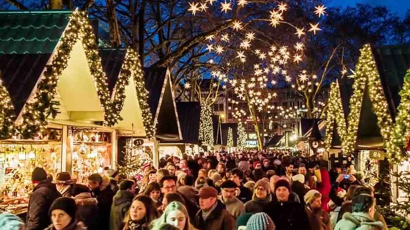 Crowded outdoor Christmas market with glowing star lights and festive stalls at night.