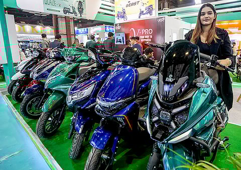 A woman poses for a picture with two-wheelers during the 23rd EVEXPO on Electric Vehicles, at Bharat Mandapam in New Delhi.