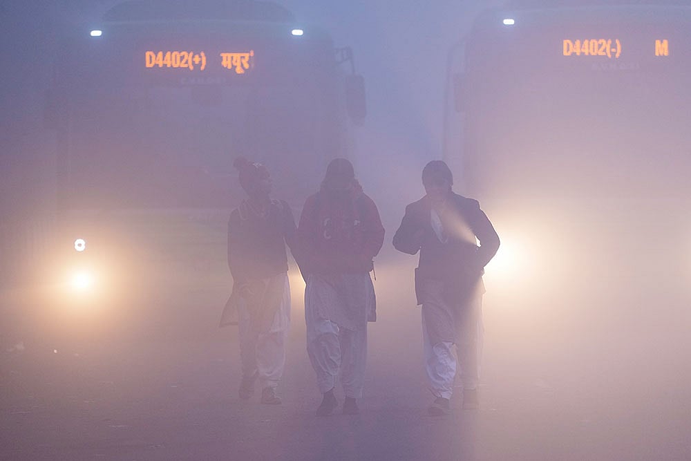 School children brave dense fog on a winter morning, at Mayur Vihar area, in New Delhi. Visibility plunged across parts of Delhi on Saturday morning, with buildings and flyovers fading into a grey blur amid dense fog, as the capital’s AQI edged closer to the ‘severe’  category at 384. - | Photo: PTI/Ravi Choudhary