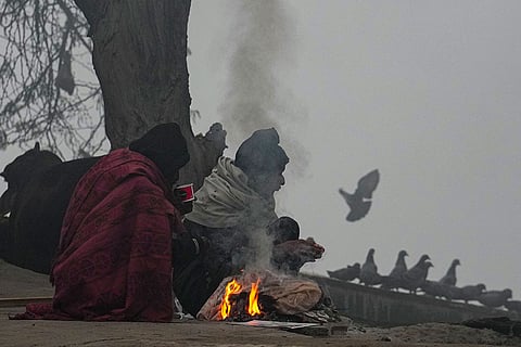 People warm themselves around a small fire on a foggy winter morning, in New Delhi.