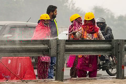 Workers clean a siderail on NH-24 with a washer gun amid dense fog on a winter morning, at Mayur Vihar area, in New Delhi.