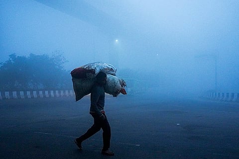 A man carrying sacks of goods walks by amid dense fog on a winter morning, at Mayur Vihar area, in New Delhi.