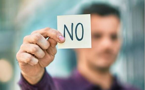 흐릿하게 보이는 한 남자가 검은색 잉크로 NO라고 쓰여진 네모난 카드를 들고 있다.