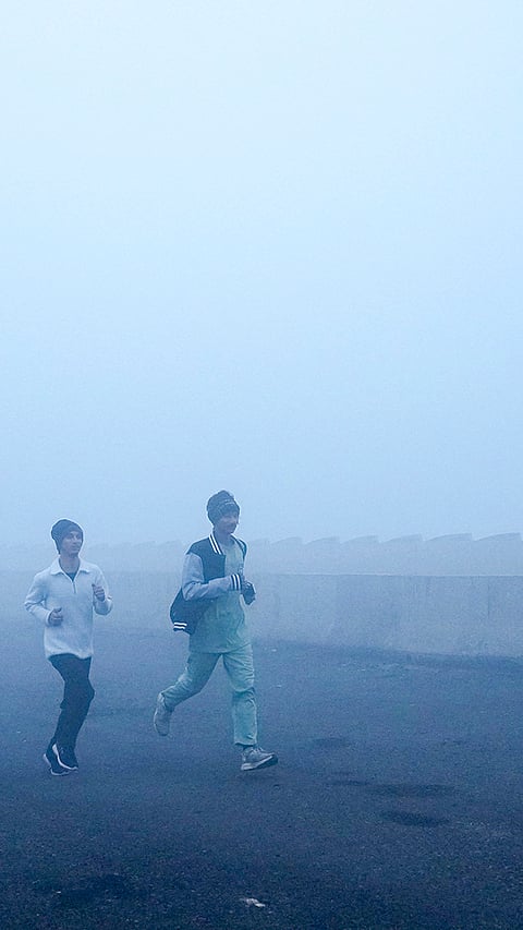 People jog amid dense fog on a winter morning, at Mayur Vihar area, in New Delhi.