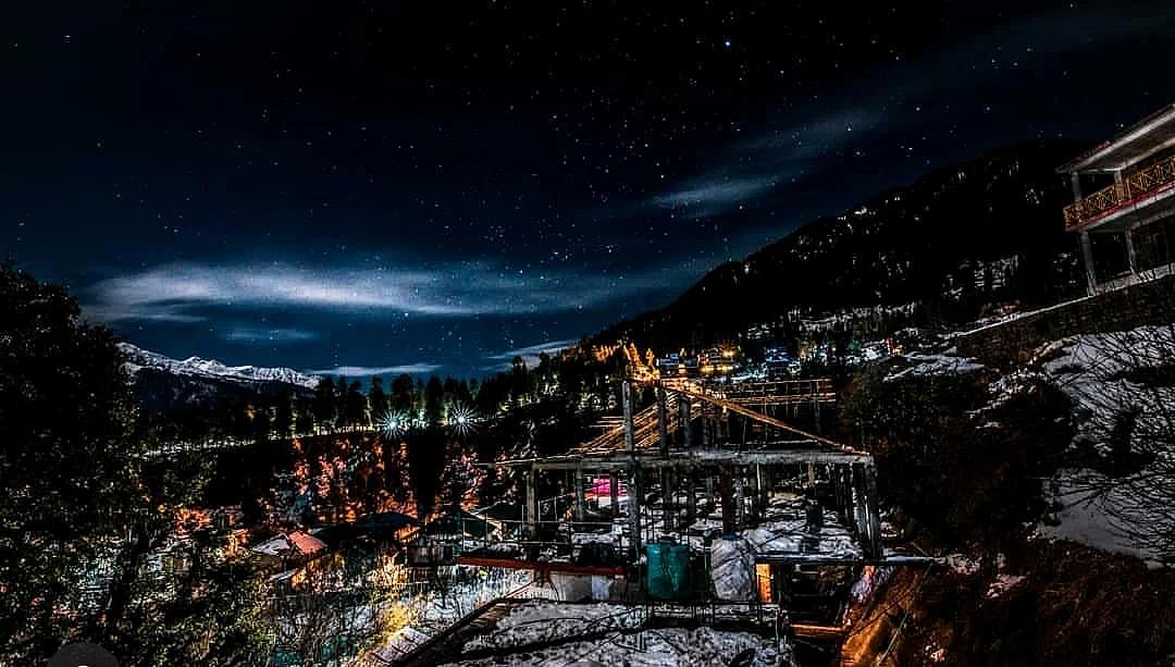 Night view of a snowy mountain village under construction with a starry sky.