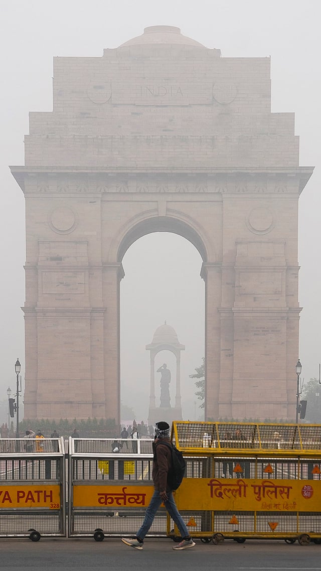 A man walks by as the India Gate remains shrouded in fog on a winter morning, in New Delhi. - | Photo: PTI/Arun Sharma