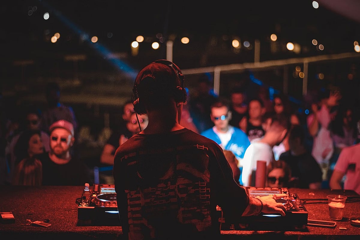 Silhouette of a DJ performing at a night club with a blurred crowd in the background.