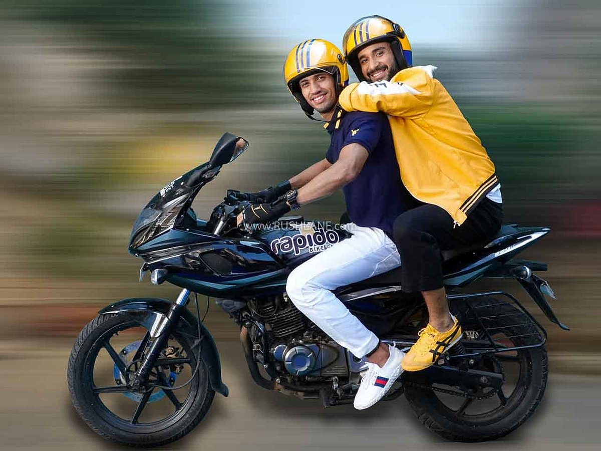 Two men wearing yellow helmets riding a blue Rapido motorcycle on a road.