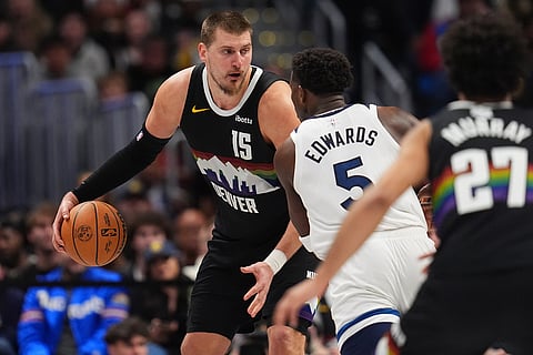 Denver Nuggets center Nikola Jokić, back, looks to pass the ball as Minnesota Timberwolves guard Anthony Edwards defends in overtime of an NBA basketball game in Denver. 