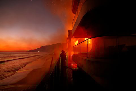 Firefighters work from a deck as the Palisades Fire burns a beachfront property Jan. 8, 2025, in Malibu, California.