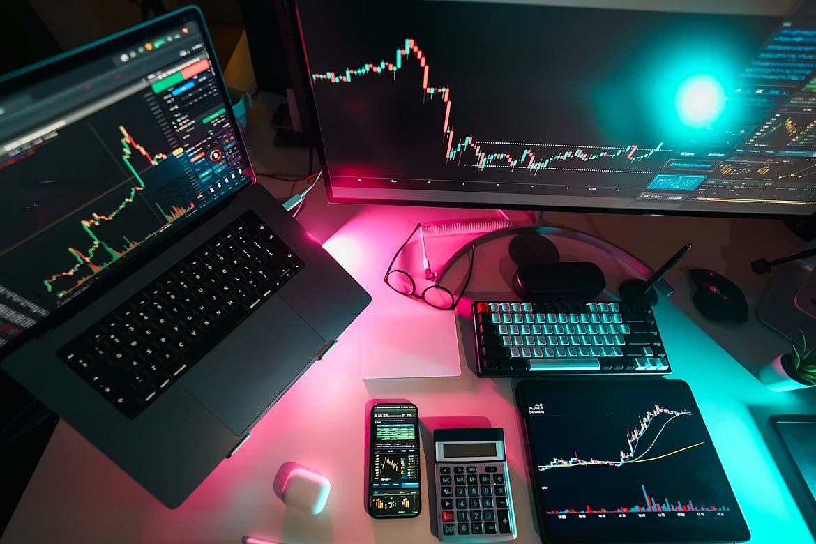 Trading desk with a laptop, monitor, and tablet displaying financial charts.
