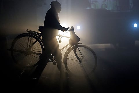 A man with his bicycle walks along a road as a dense layer of fog blankets the area, affecting visibility on a winter morning, in New Delhi.