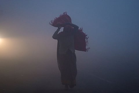 A person walks along a road as a dense layer of fog blankets the area, affecting visibility on a winter morning, in New Delhi.