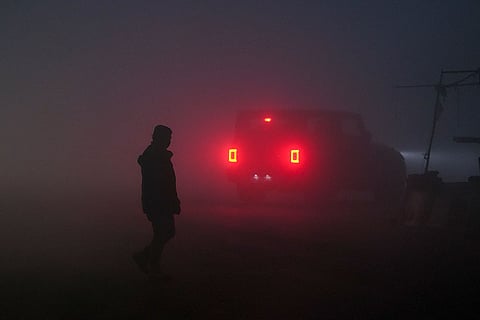 A person crosses a road as a dense layer of fog blankets the area, affecting visibility on a winter morning, in New Delhi