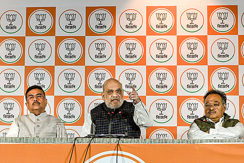 Union Home Minister Amit Shah, centre, during a press conference, in Kolkata, Tuesday, Dec. 30, 2025. West Bengal Leader of Opposition Suvendu Adhikari, left, with state BJP President Samik Bhattacharya are also seen. 