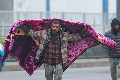 A man covers himself with a blanket on a cold winter morning, in New Delhi.