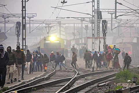 People cross railway tracks amid low visibility on a foggy winter morning, in Patna.