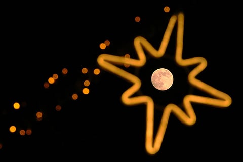 The full moon, known as the Wolf Supermoon, rises near decorative lights along a street, in Beijing.