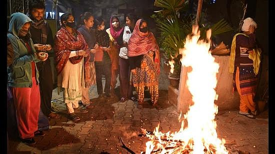 People standing in traditional attire around a large, glowing bonfire during a Lohri celebration.