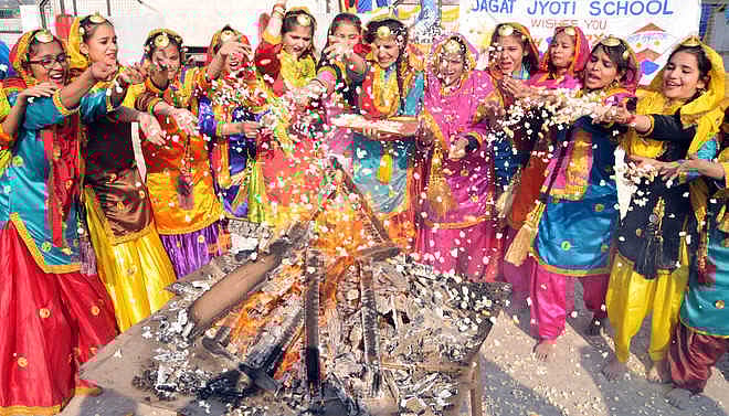 A group of women in colorful traditional Punjabi suits celebrating around a large bonfire.